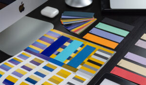 Purple, yellow, and blue color swatches on a table, with iMac computer and Apple AirPods