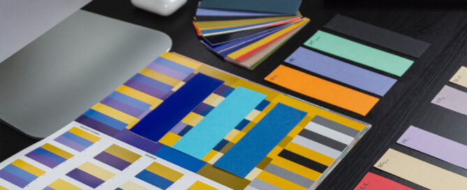 Purple, yellow, and blue color swatches on a table, with iMac computer and Apple AirPods