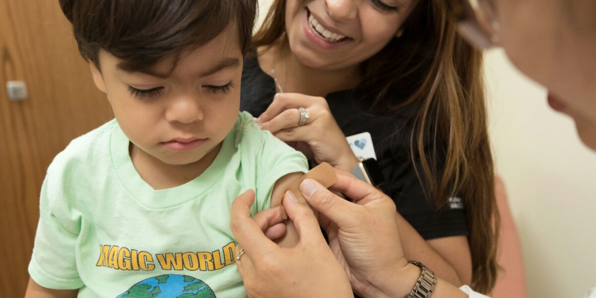 child getting bandaid put on by two smiling healthcare professionals