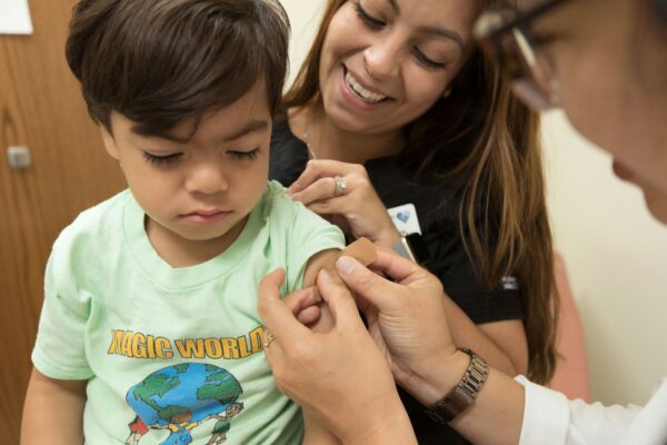 child getting bandaid put on by two smiling healthcare professionals