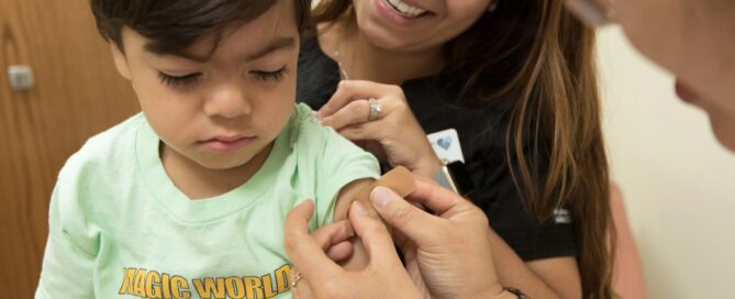 child getting bandaid put on by two smiling healthcare professionals