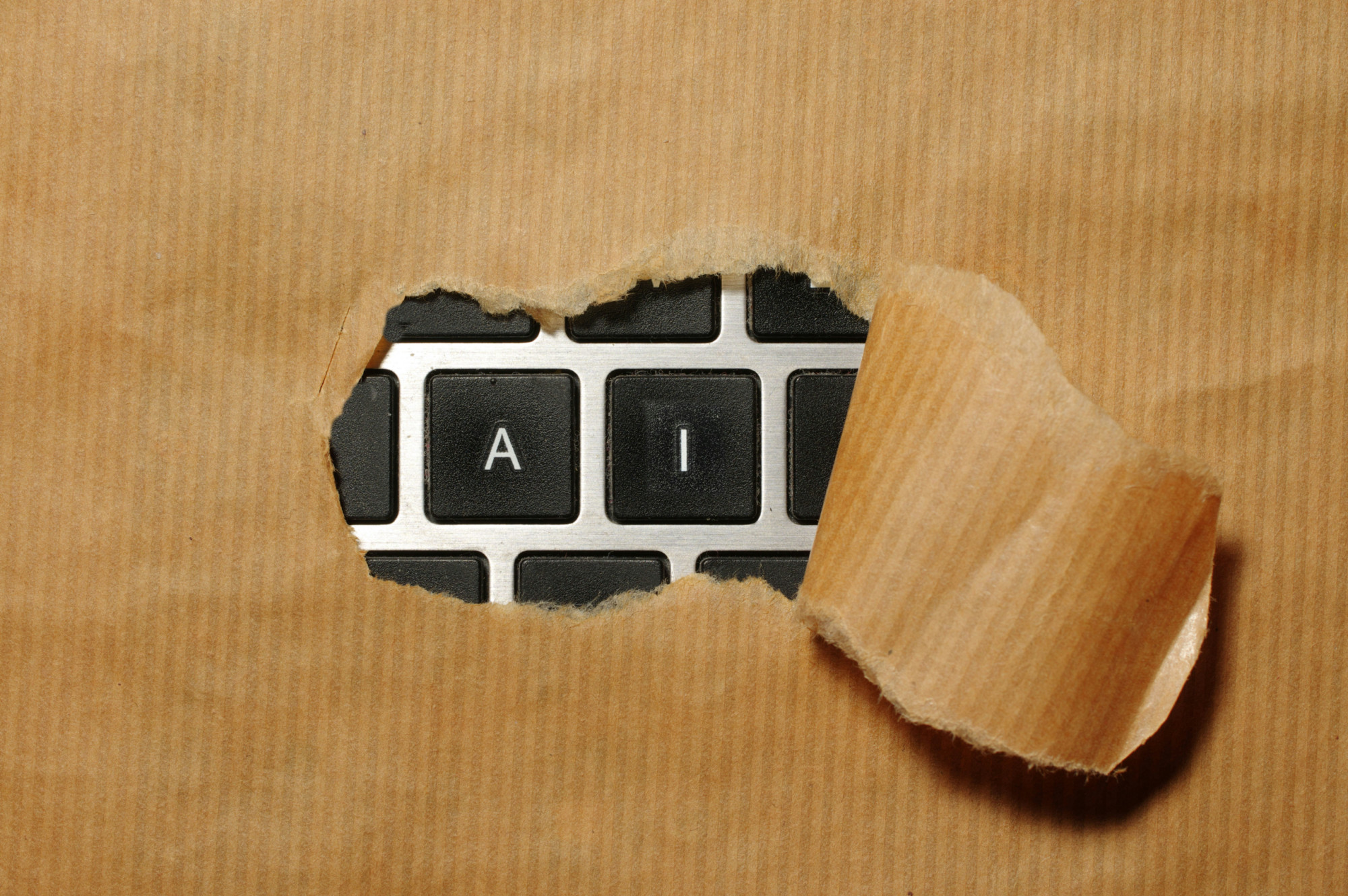 Brown kraft paper torn open to reveal a laptop keyboard with the A and I keys visible